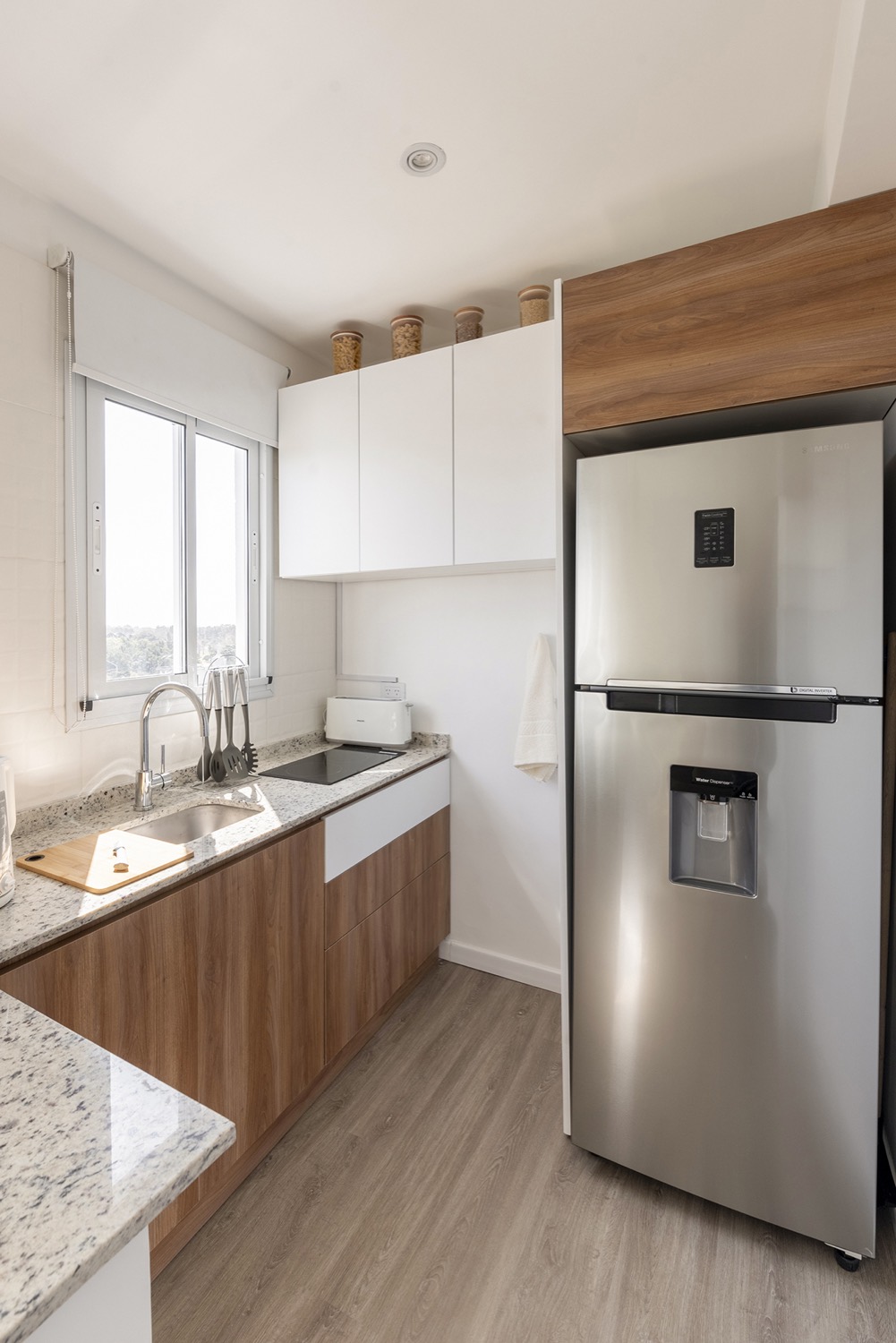 Cocina del departamento India con alacenas blancas, bajomesadas de madera y mesada de piedra clara