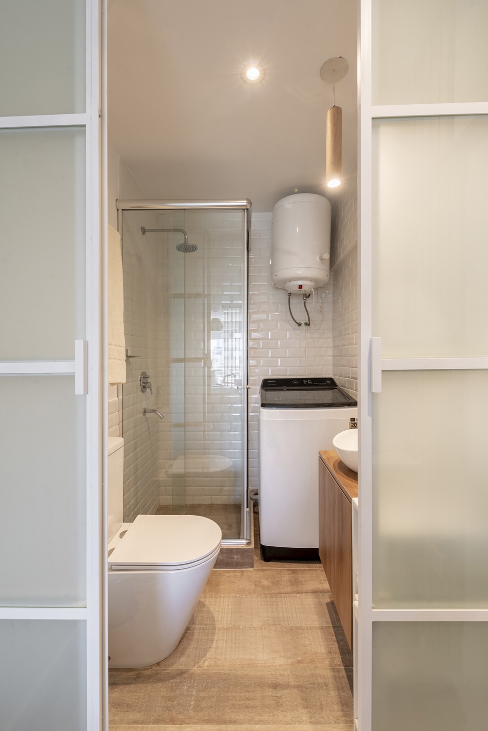 Baño del departamento India con tabique vidriado y mueble bajo mesada de madera