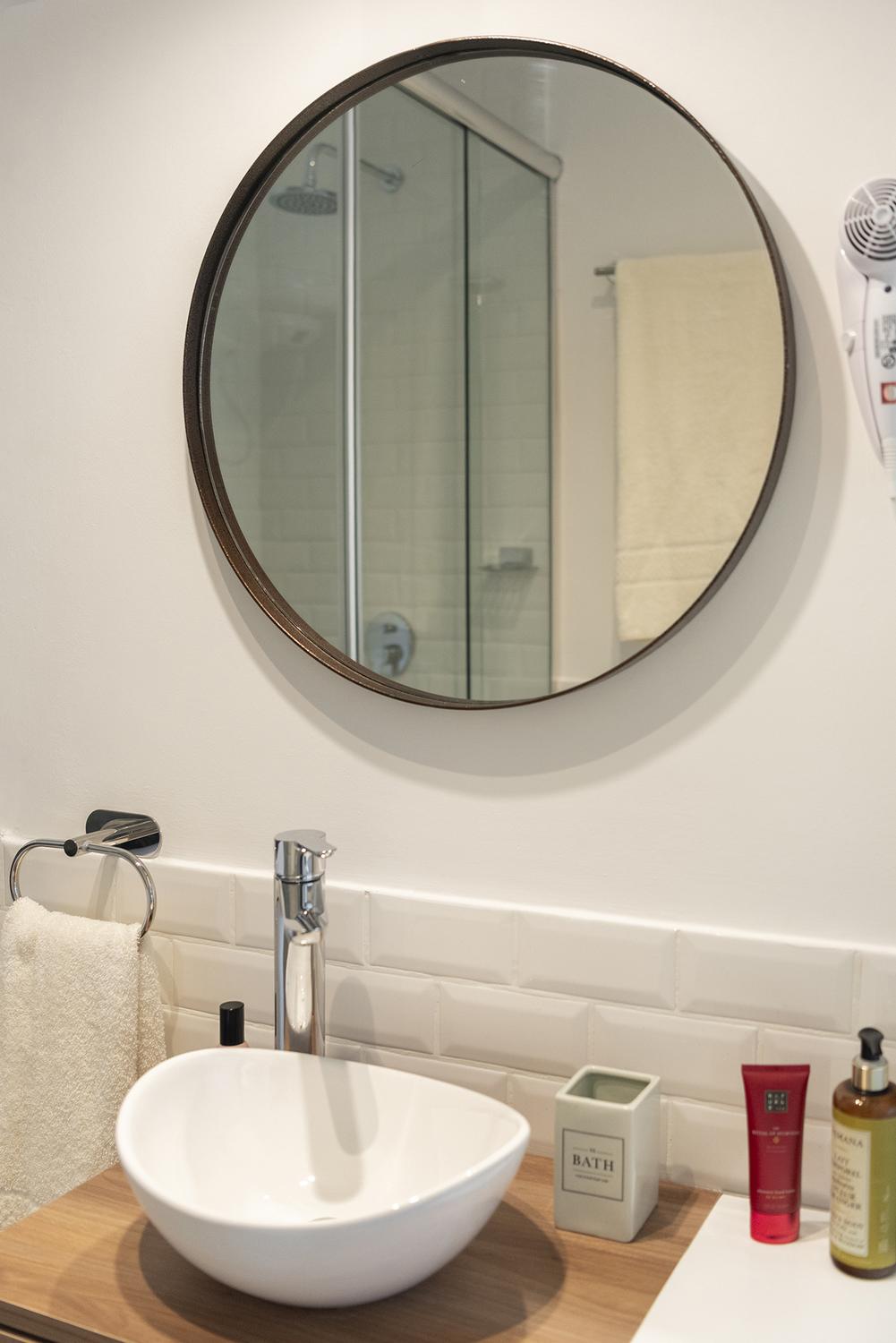 Espejo redondo, bacha de apoyar y amenities en el baño del monoambiente India