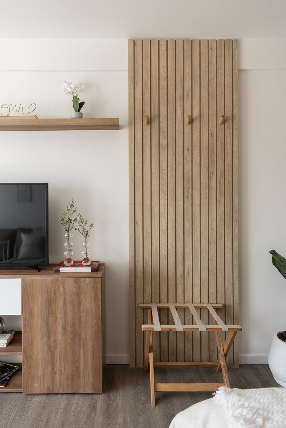Frente de lamas de madera con perchero y banqueta, y la televisión sobre un mueble bajo