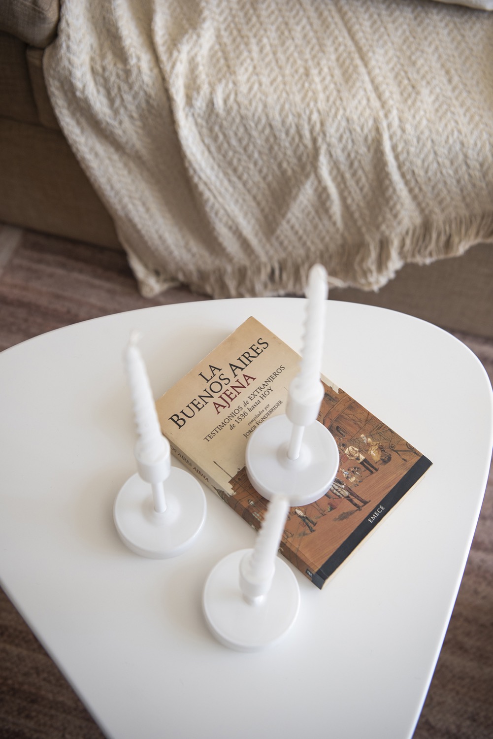 Detalle de la mesa baja blanca del estar con un libro y candelabros