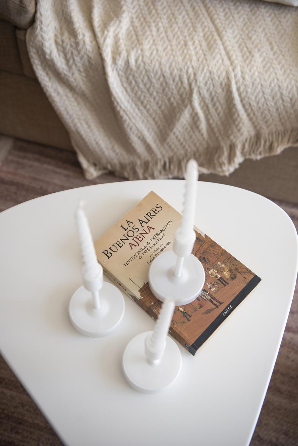 Mesa baja del estar con un libro sobre Buenos Aires y tres candelabros blancos