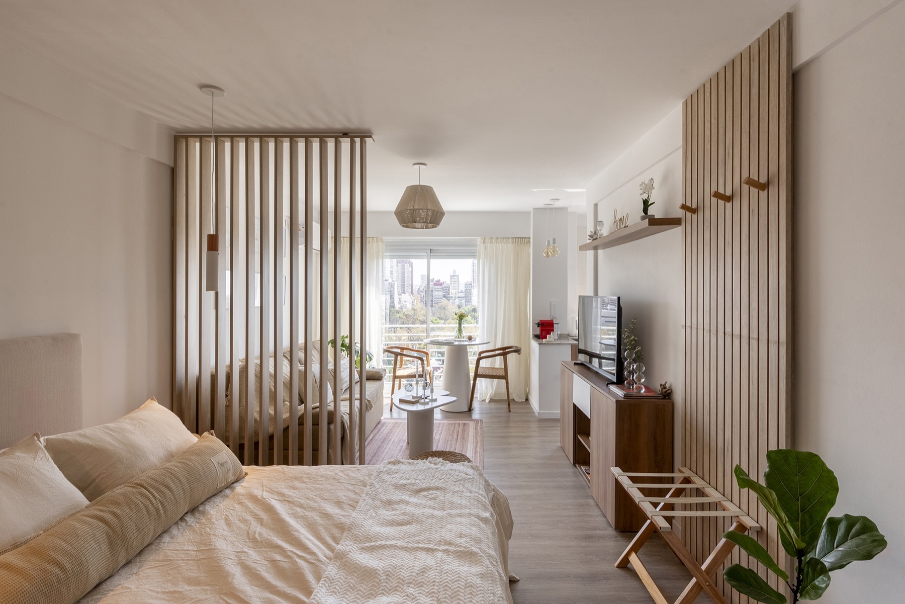 Dormitorio del departamento India detrás de un tabique de lamas verticales de madera clara, con el estar al fondo