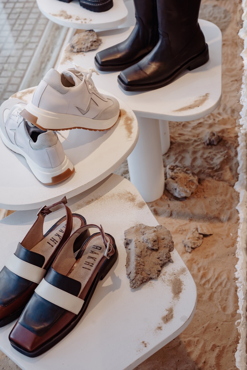 Detalle de una bandeja de exhibición curva con sandalias y una piedra natural como contrapunto