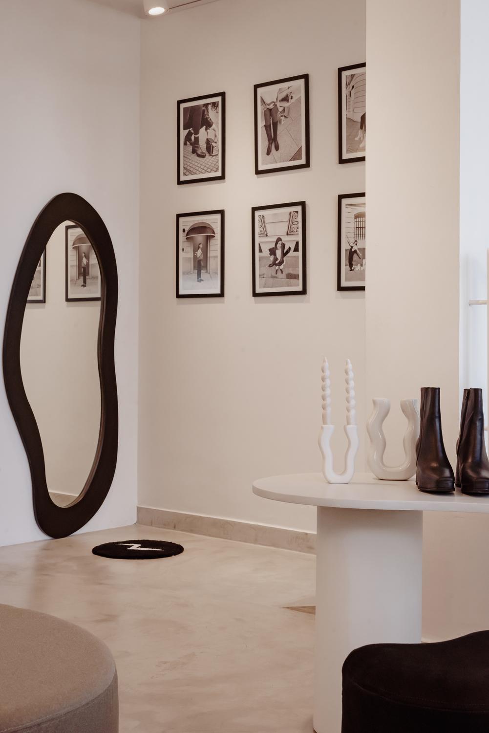 Sala blanca de Rakhi con espejo de contorno irregular y una serie de fotografías enmarcadas