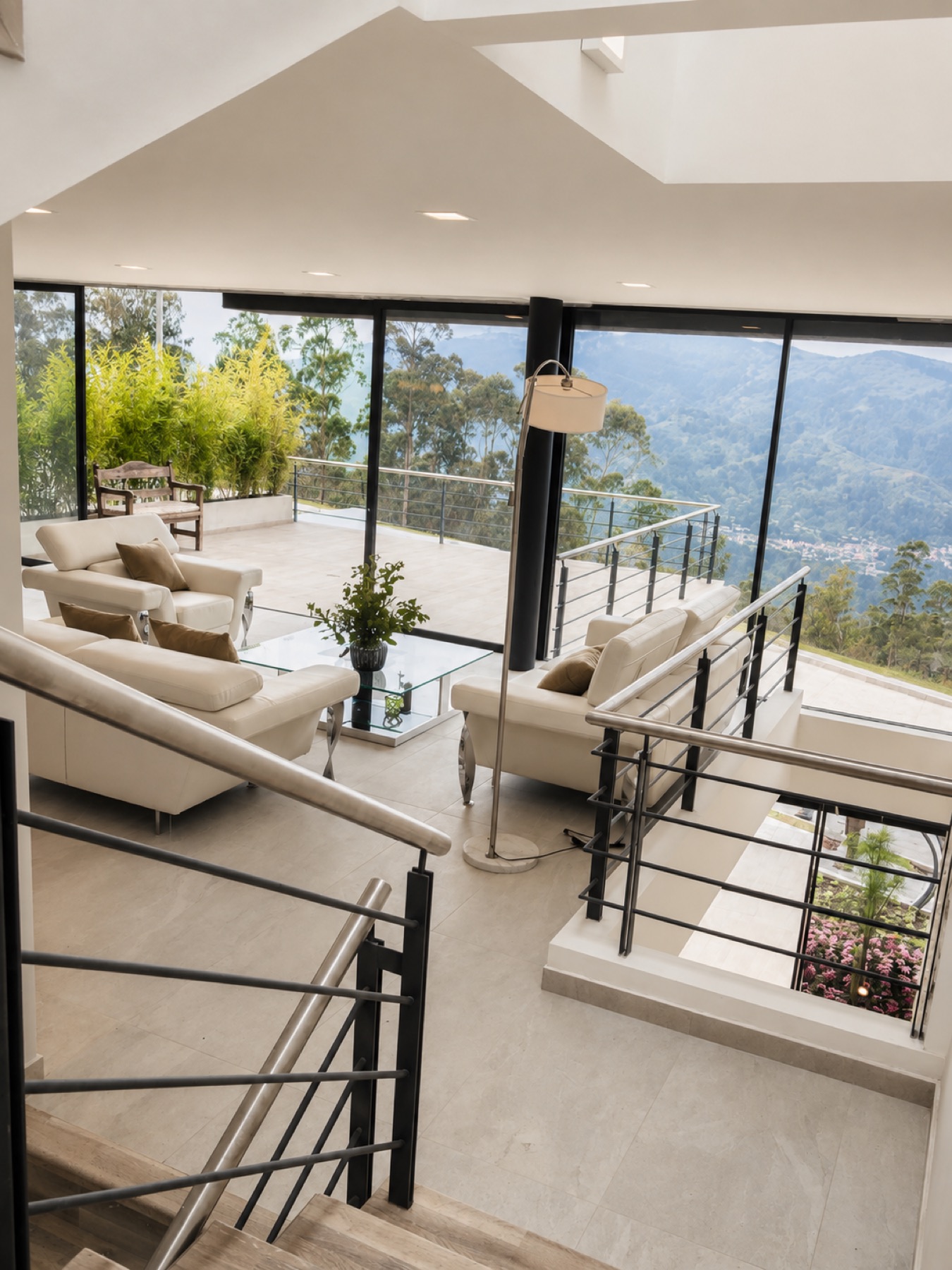 Estar de doble altura de la casa Sevillana, con ventanal de acero negro, balcón interior y vista a la montaña